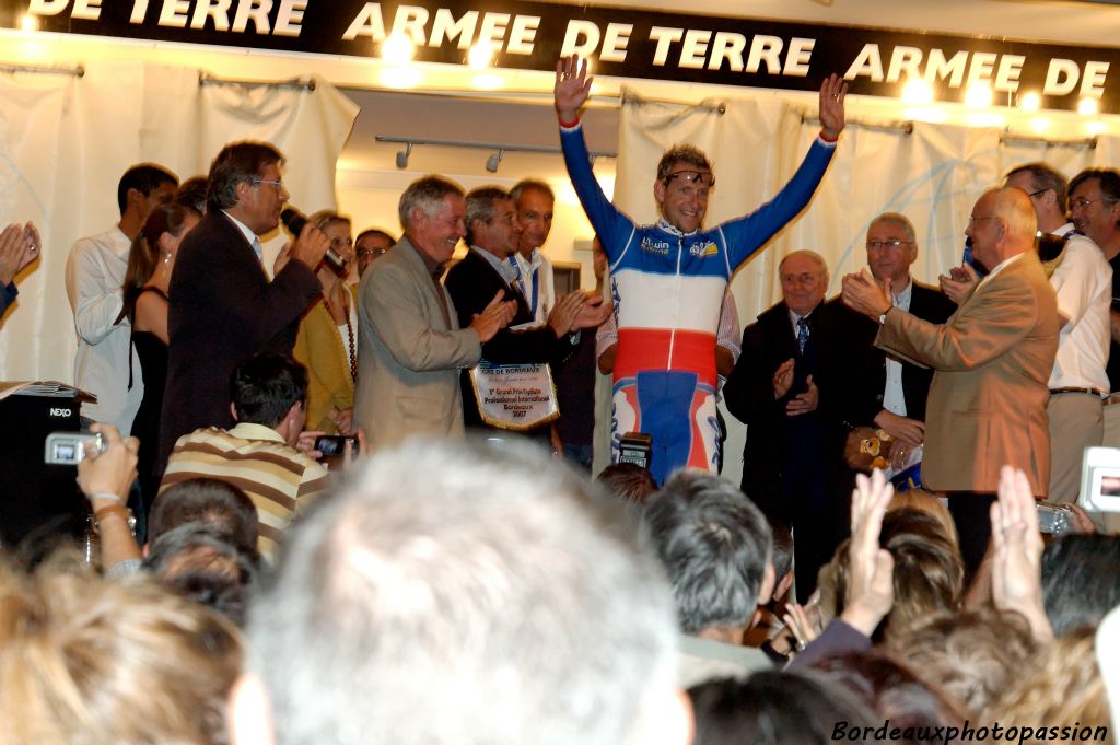 Il s'appelle Christophe Moreau. Il est champion de France de cyclisme professionnel. Il lève les bras en signe de victoire.