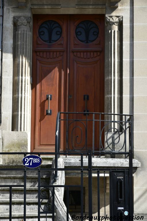 Deux colonnes rainurées avec chapiteaux stylisés encadrent la porte en bois à deux battants.