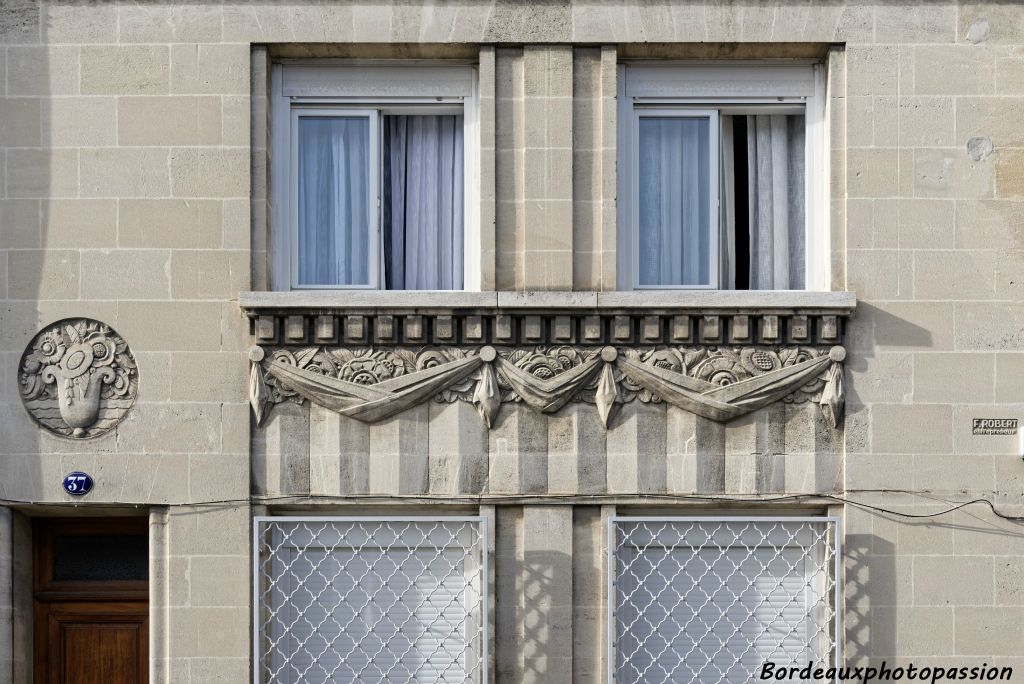 La décoration sous les fenêtres est composée d'une frise de denticules, de panneaux décoratifs en méplat masqués par des "tissus" posés sur un éventail simple.