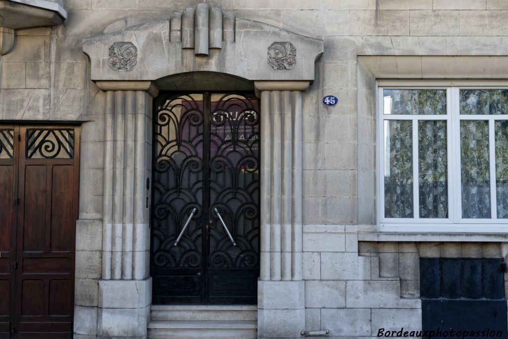 La ferronerie de la porte participe grandement à la décoration. Elle est encadrée par des colonnes engagées et un fronton décoré de tubulures.