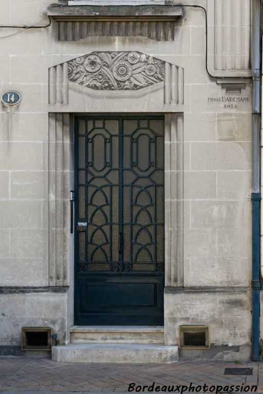 La ferronerie aux motifs Art Déco est mise en valeur par des pseudo-pilastres. Un linteau décoré d'un panneau décoratif à pans coupés en méplat rappelle les ouvertures de l'étage.